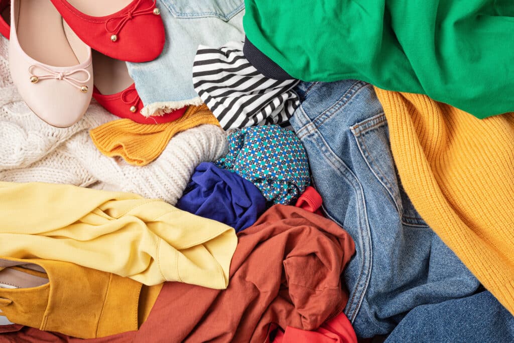 Fast fashion background with pile of cheap, low quality clothes. Garment made in unjust, inhumane conditions idea. Environmental impact, carbon emissions concept